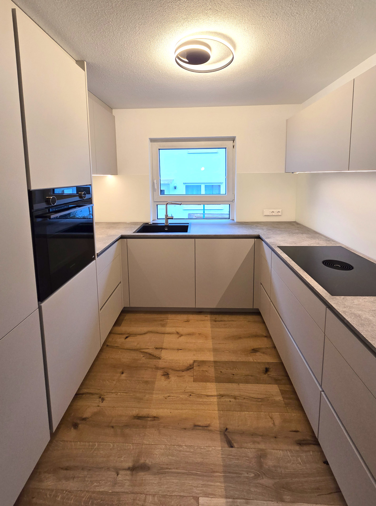 Küche mit grauer Oberfläche und Beleuchtung unter den Oberschränken individuell von Schreinerei Deuble gefertigt