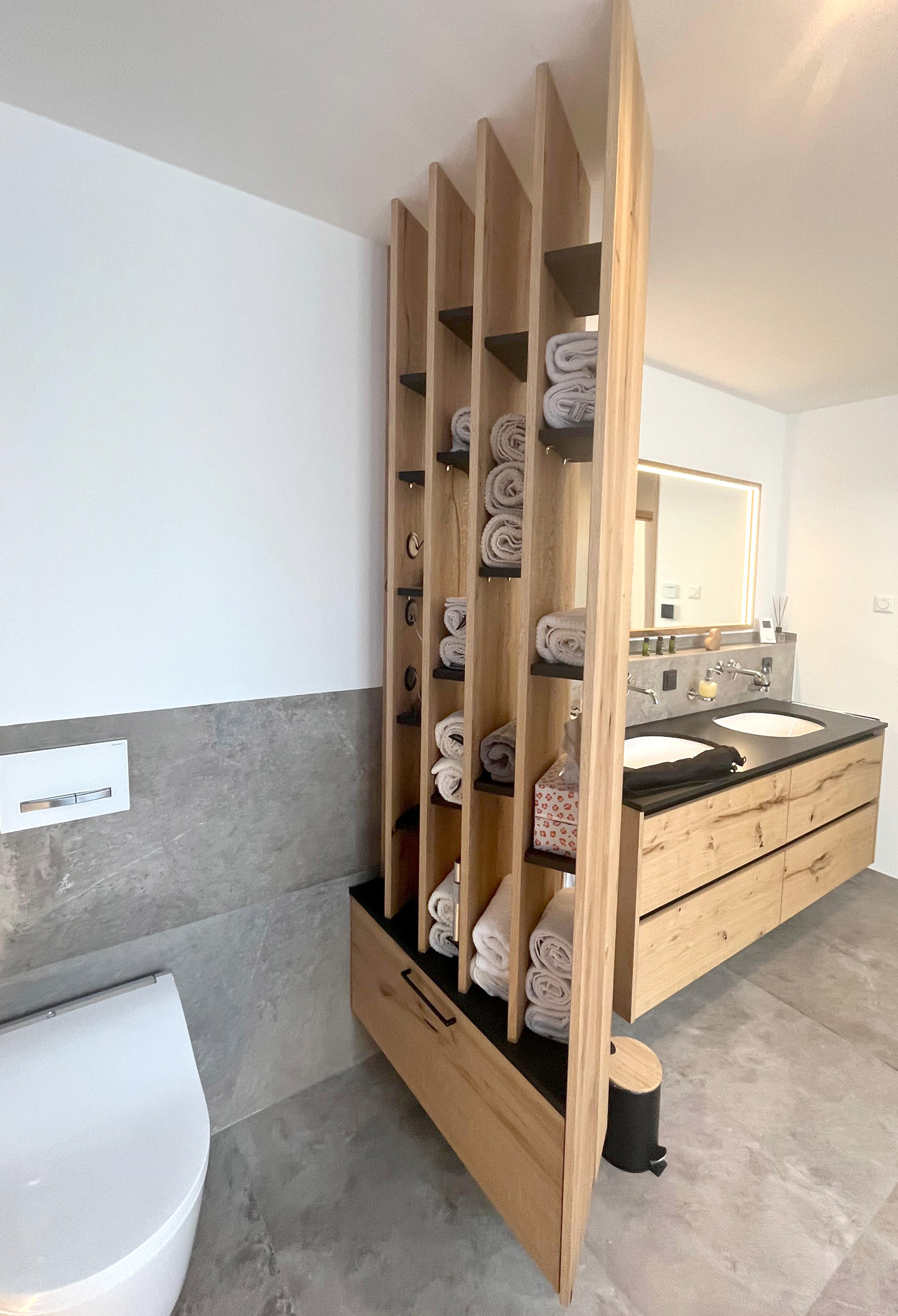 Raumtrenner aus Risseiche. Waschbeckenunterschrank mit durchgehender Optik der Front und in Steinplatte eingelassene Waschbecken.